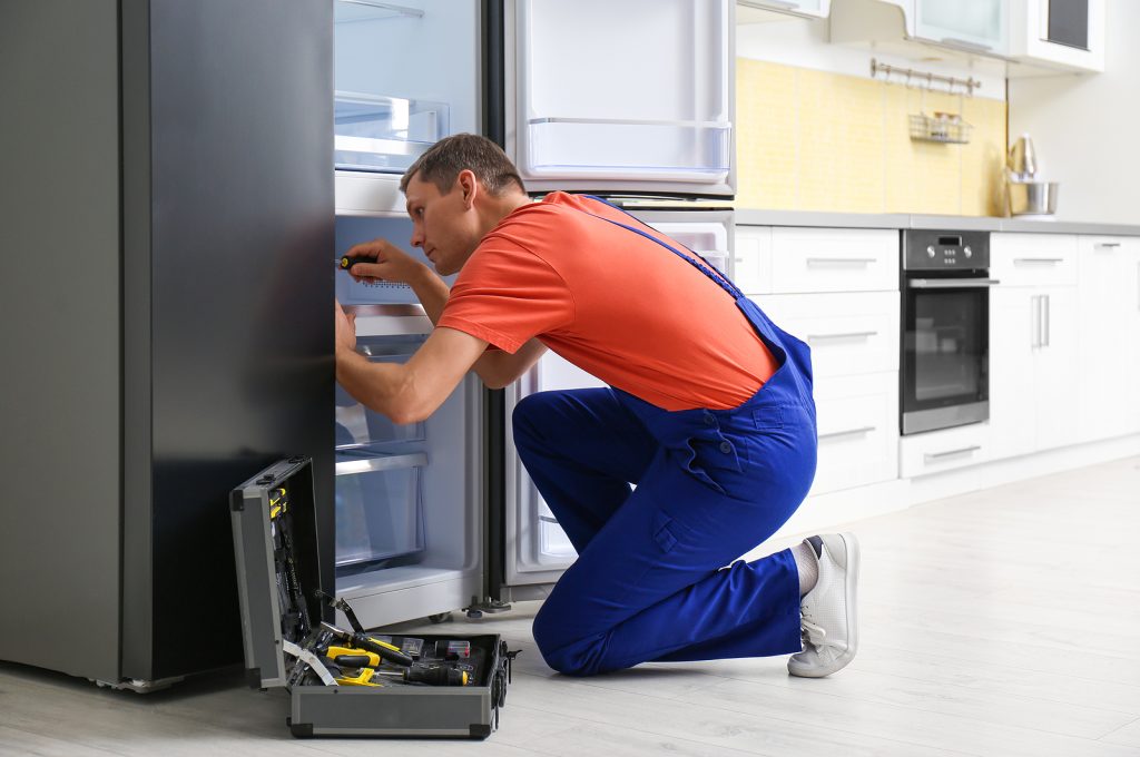 male technician with screwdriver repairing refrigerator in kitch